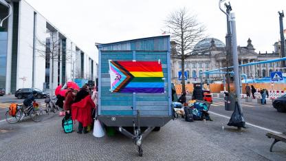 Ein Saunawagen mit Regenbogenflagge steht zwischen Paul-Löbe-Haus und Bundestag